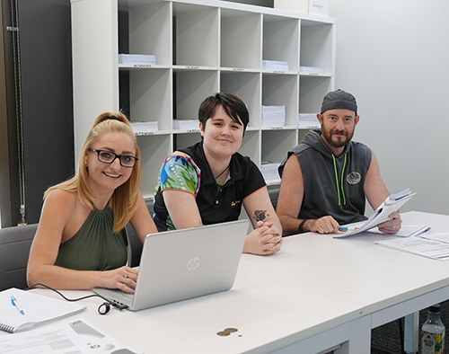 Three people sitting at desk, with Trainer in between smiling.
